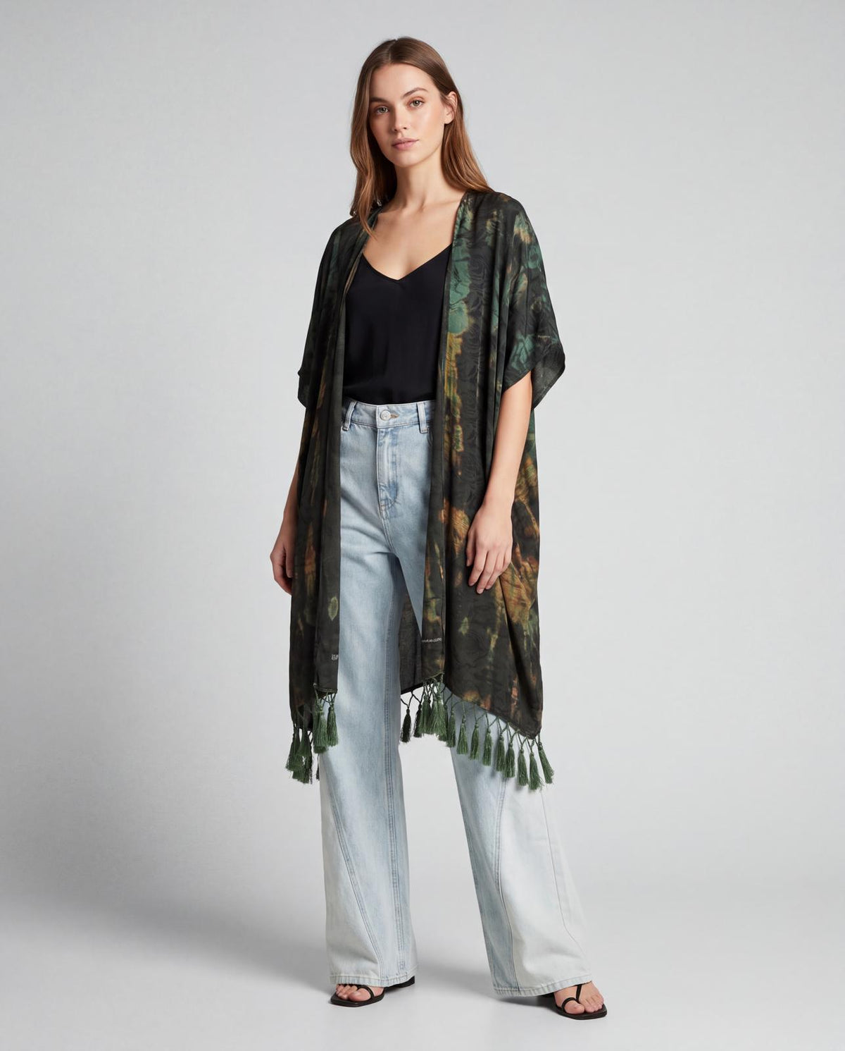 Poncho Cofur en soie de sari upcyclée porté ouvert sur un caraco noir et un jean clair, tie and dye kaki et rouille, ourlet à pompons