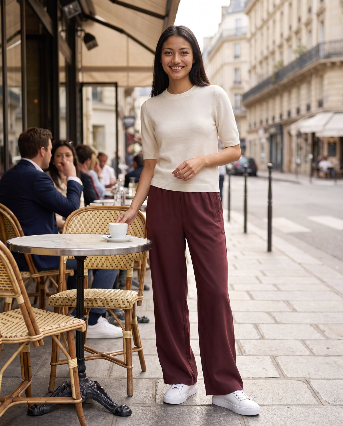 Femme portant le pantalon fluide LANIUS Bordeaux avec un t-shirt en cachemire blanc dans un café parisien – lifestyle