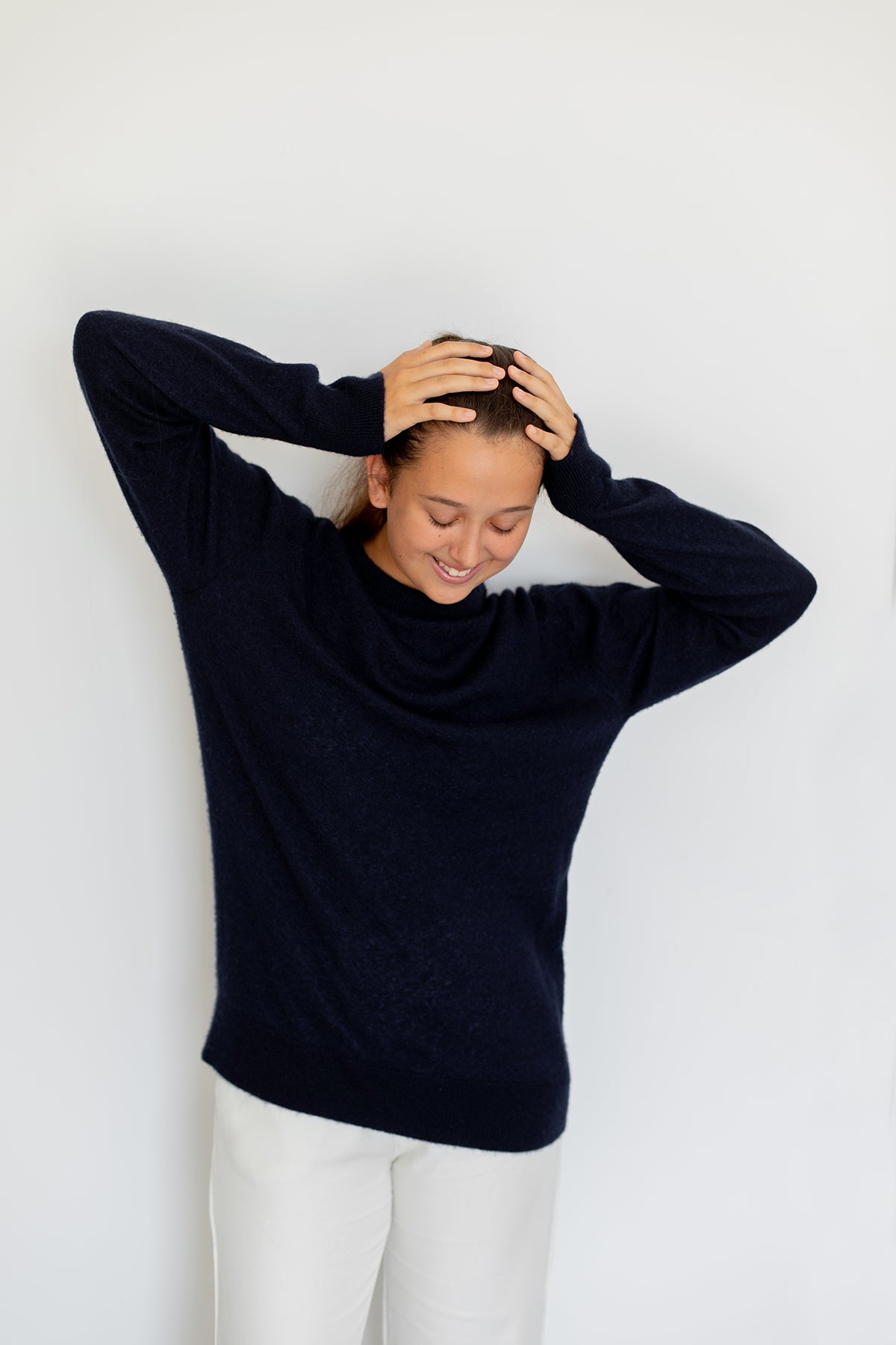 Pull col rond Nuage Cashmere en Indigo, porté de trois quarts, main dans les cheveux