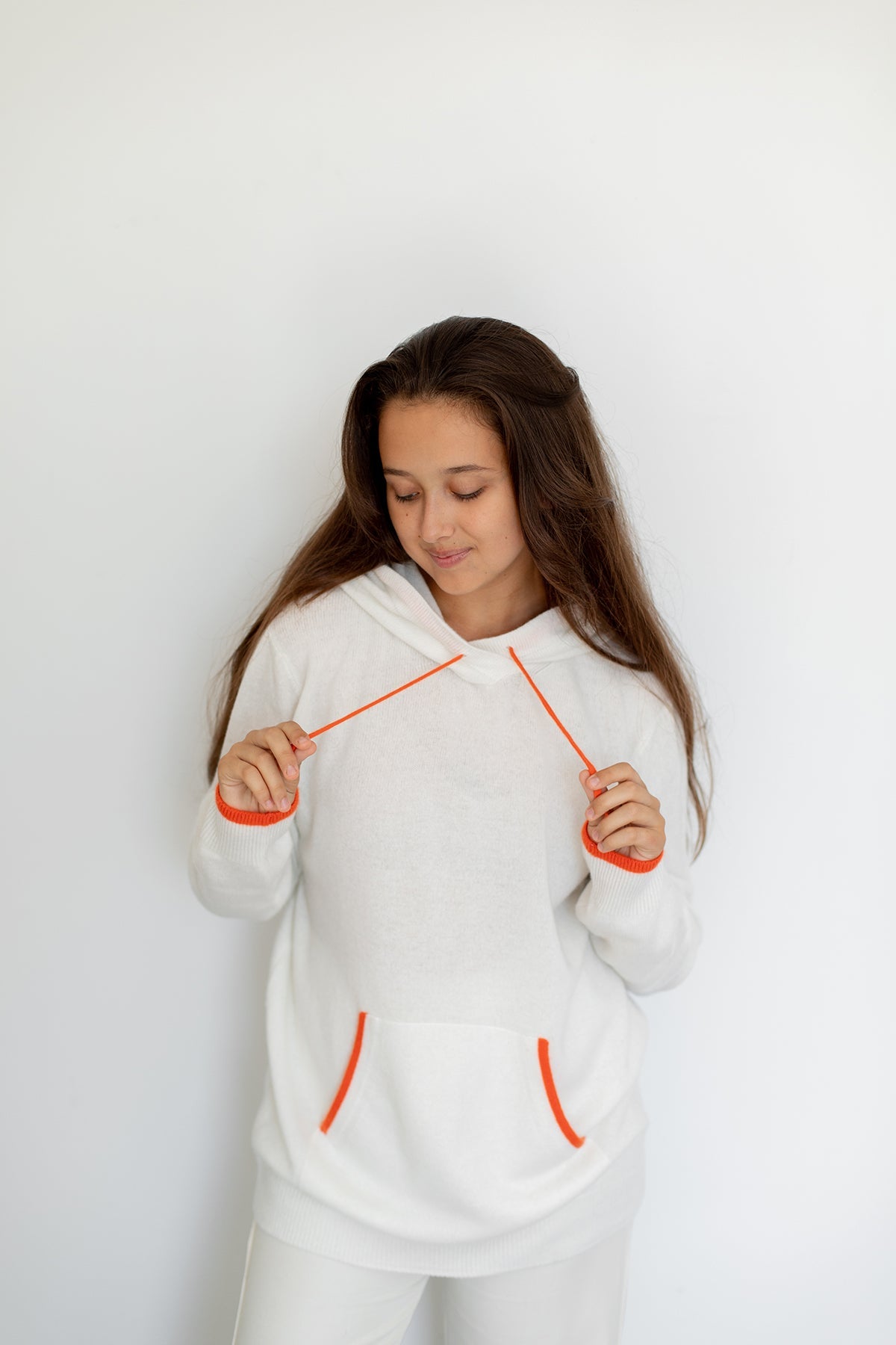 Sweat à capuche Nuage Cashmere en White Angel, porté de face, mains sur les cordons orange