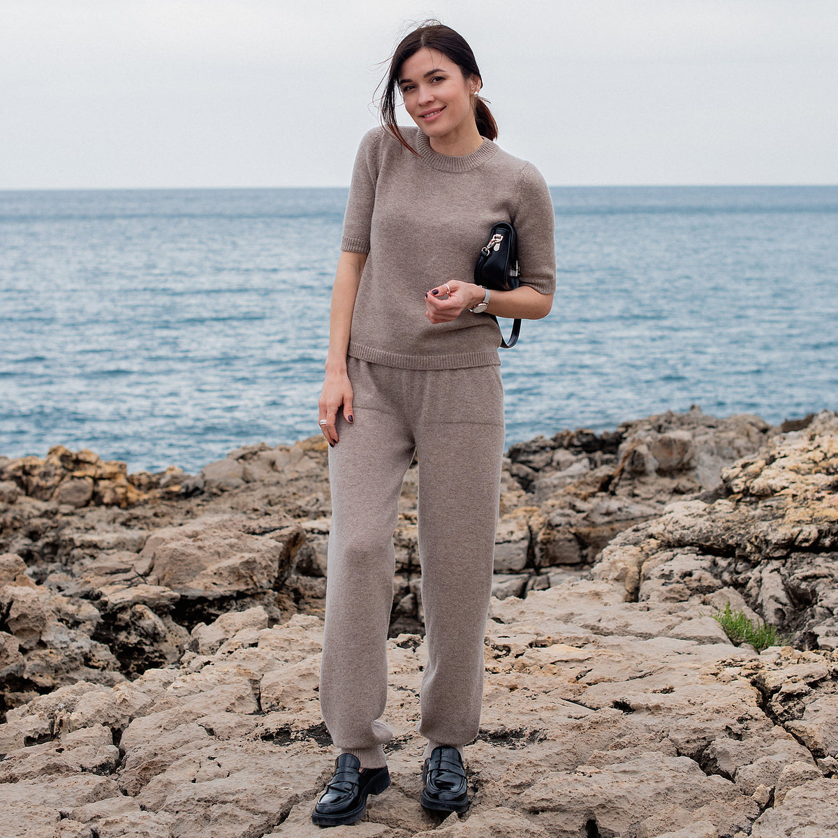 T-shirt en cachemire Nuage Cashmere Cappuccino, porté en pied au bord de la mer
