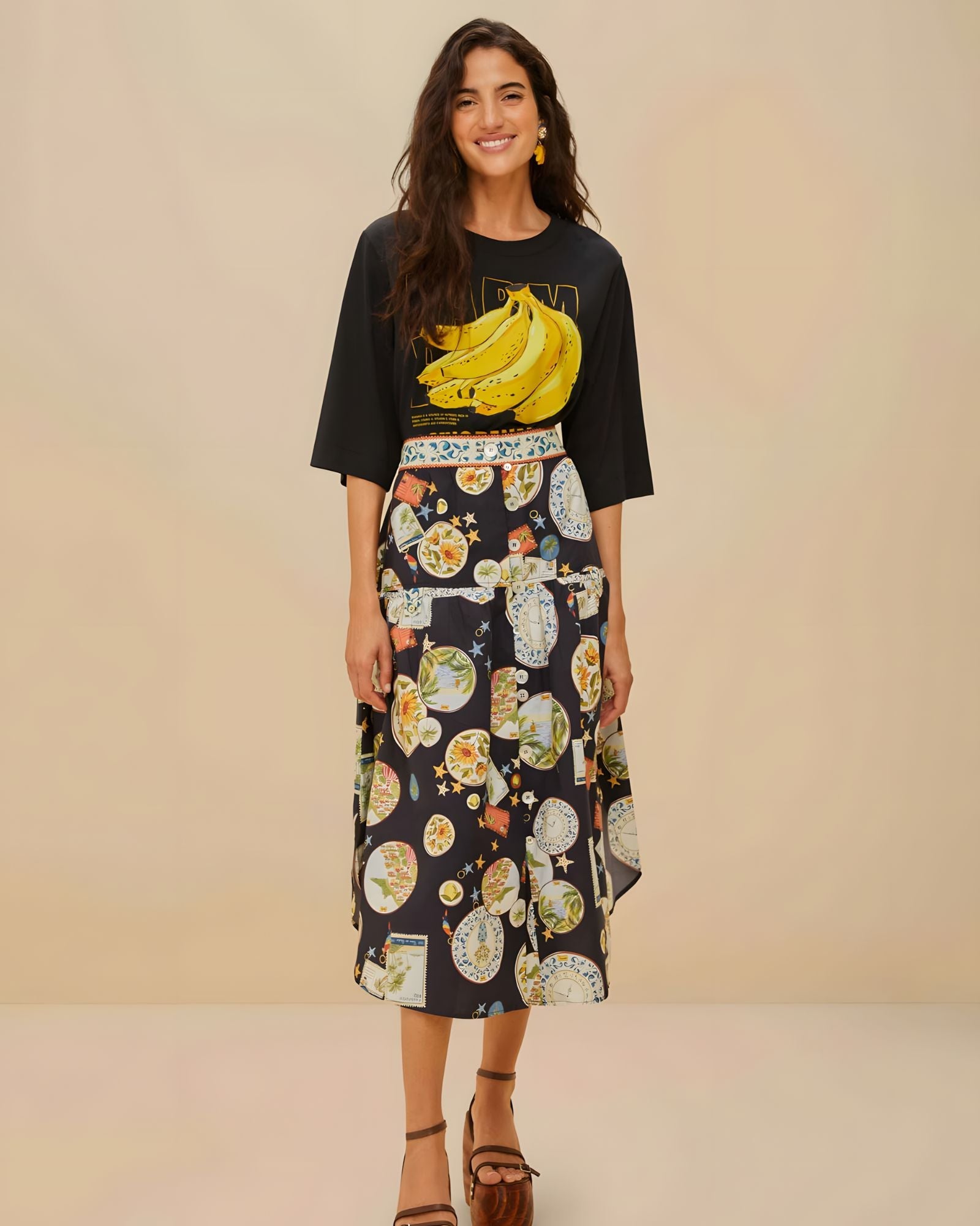Mannequin en pied portant le t-shirt Going Bananas de FARM Rio associé à une jupe midi imprimée à motifs voyage et des sandales à talons