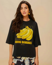 Mannequin portant le t-shirt noir Going Bananas de FARM Rio, imprimé bananes jaune visible sur le devant, boucles d'oreilles pendantes jaunes, vue portrait