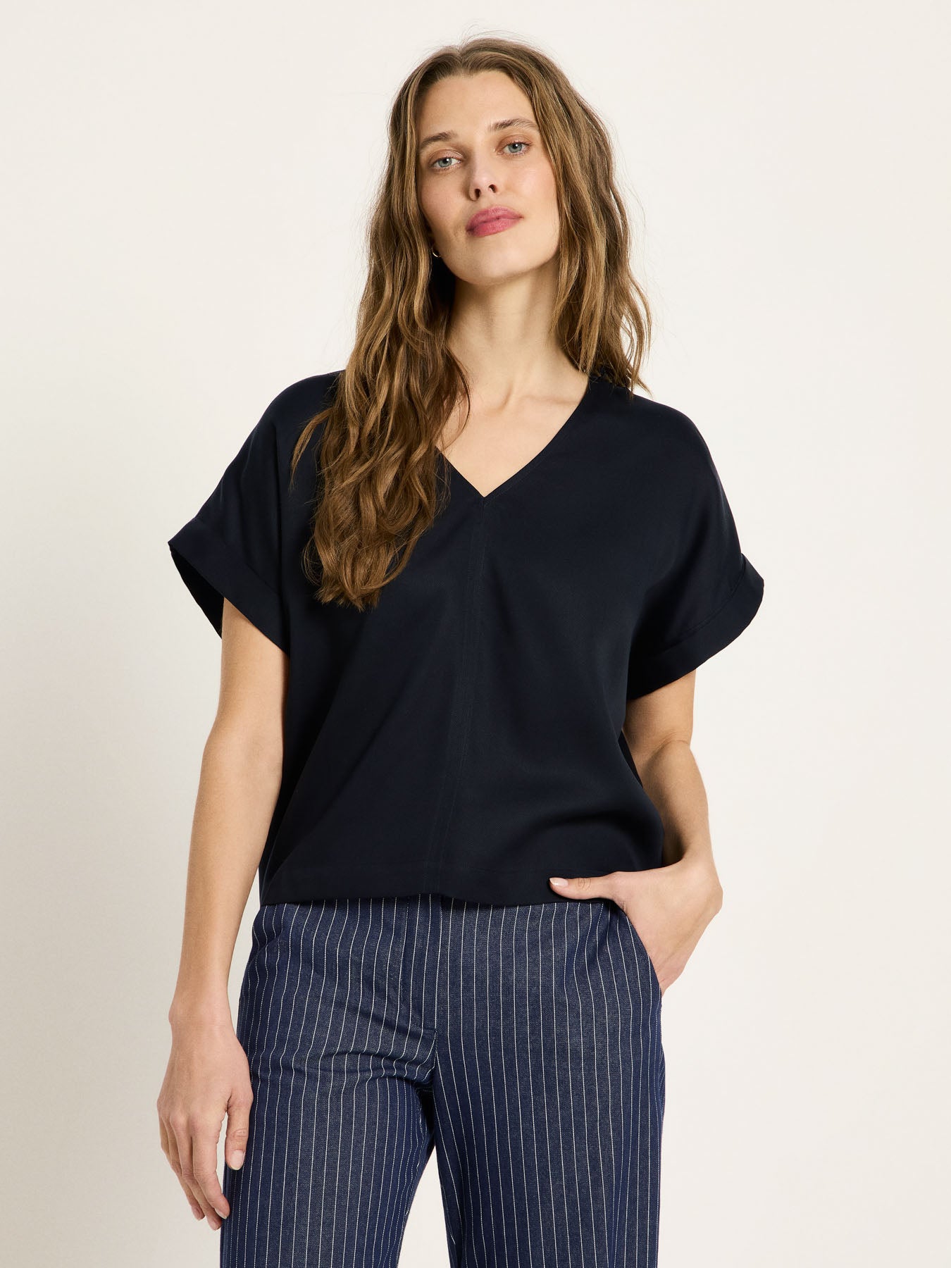 Mannequin portant le haut drapé col en V bleu nuit LANIUS, une main en poche, associé à un pantalon rayé bleu marine et blanc