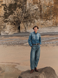 Jean barrel Ember LANIUS Denim bleu moyen porté avec une chemise en jean, sur les rochers d’une plage