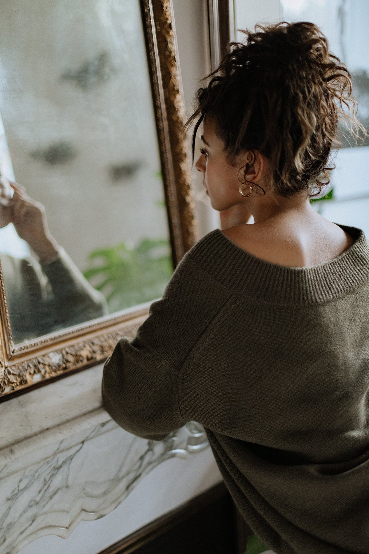 Pull col V Iconic Nuage Cashmere en Olive, porté de trois quarts dos devant un miroir
