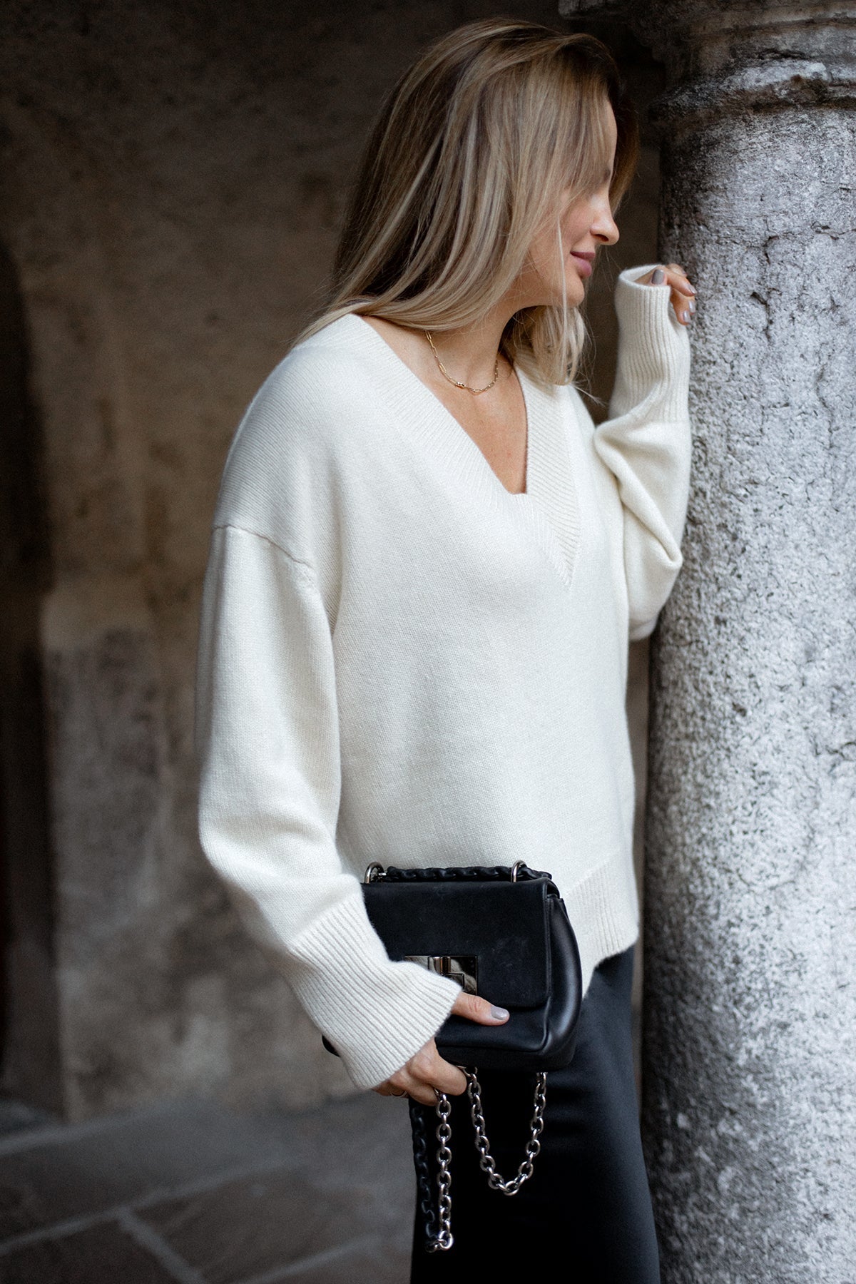 Pull col V Iconic Nuage Cashmere en Vanilla, porté de profil contre une colonne