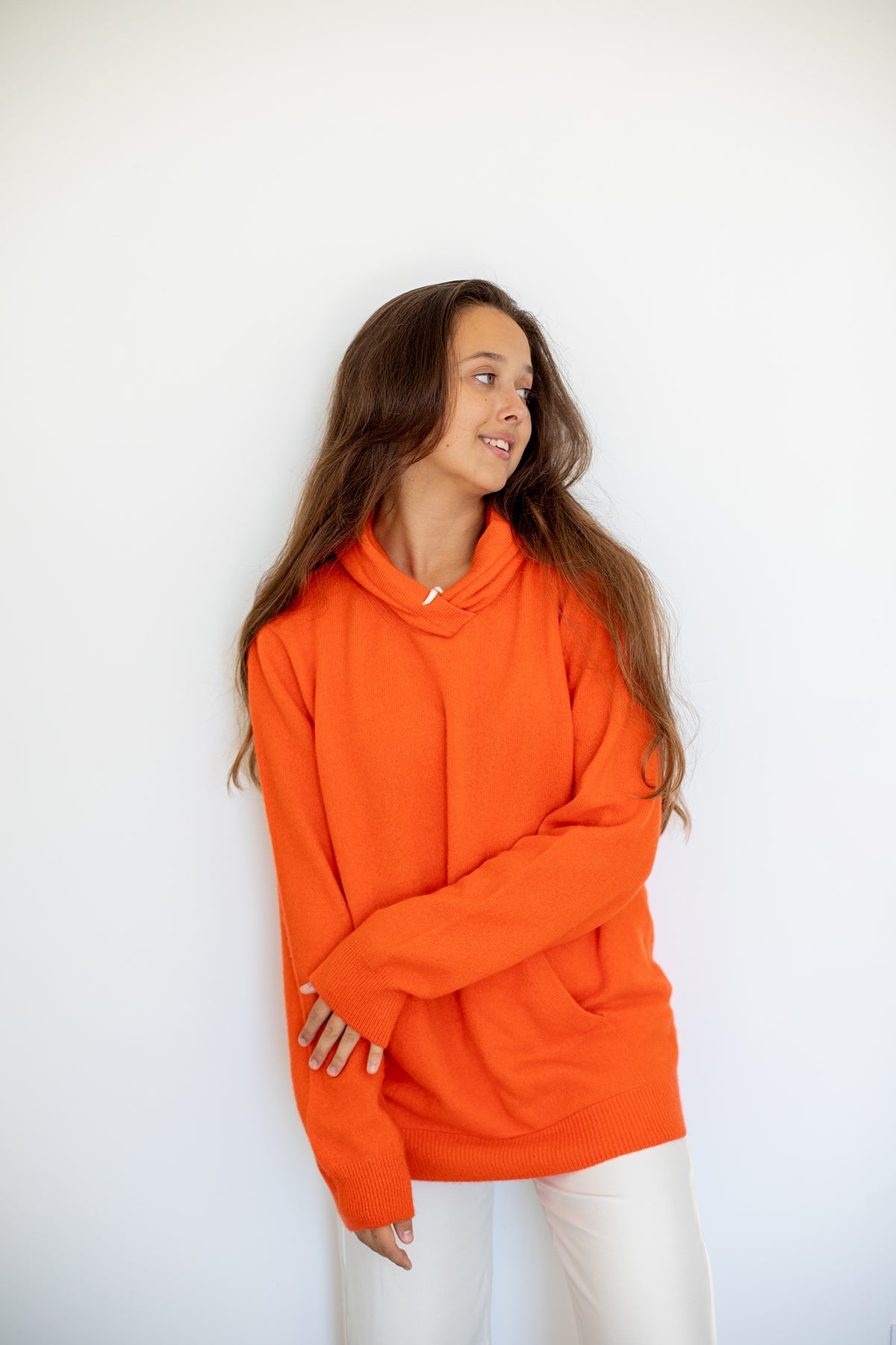 Sweat à capuche Nuage Cashmere en Aperol, porté de profil sur un pantalon blanc