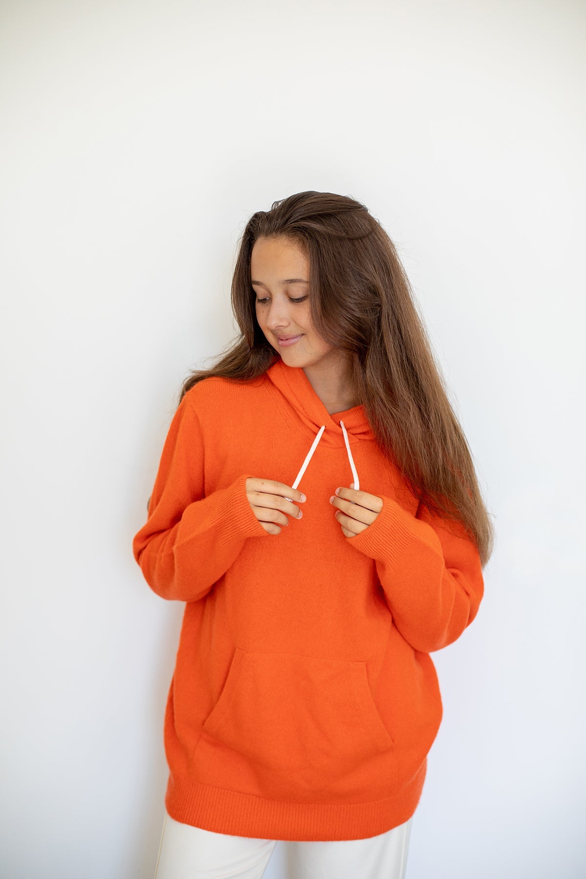 Sweat à capuche Nuage Cashmere en Aperol, porté de face, mains sur les cordons